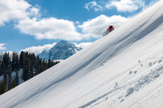 Stock picture of a freeride skier that is skiing fast downhill in deep powder snow. Big mountains and blue sky in the background. The location is Lofer in Austria