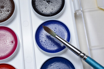 multicolored paints for drawing in a palette and a brush. on a light background close-up.