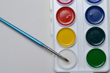 multicolored paints for drawing in a palette and a brush. on a light background close-up.