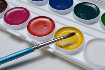 multicolored paints for drawing in a palette and a brush. on a light background close-up.