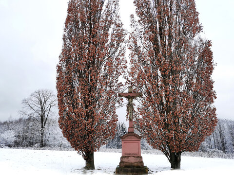 Kruzifix als Altar im Schnee zwischen zwei Bäumen