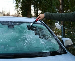 Man cleans the windshield of ice withe ice scraper .