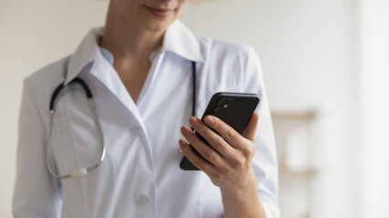 Close up focus on smartphone in young doctor hands. Focused female general practitioner giving online consultation to patient using mobile messenger applications, distant communication service concept