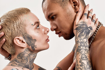 Multicultural relationship. A topless dark-skinned tattooed man and a white pierced and tattooed woman looking into eyes of each other while embracing each other