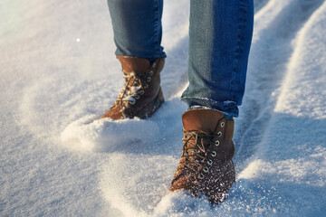 Human legs in comfortable leather brown waterproof boots in fresh snow. Casual fashion, trendy...