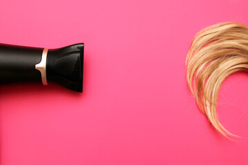 Top view of a hair dryer and a lock of hair on a pink background. Flat lying, minimalism.The concept of hair care.