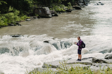 Young man with backpack traveller, taking photos of river Prut in Yaremcha, Ukraine