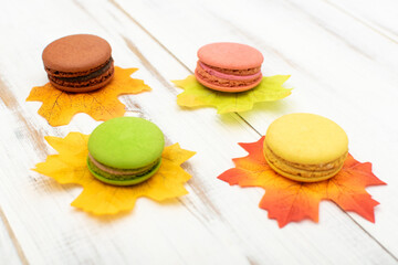 Macaroni cakes and autumn leaves on a wooden background.