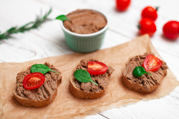 Chicken liver pate. Sandwiches, canapes with pate with cherry tomatoes on a white wooden background.