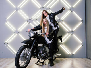 Fototapeta na wymiar Two beautiful girls wearing costumes of racers and sitting on a motorcycle, in the studio