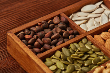 Different kinds of nuts and dried seeds in wooden box on brown wooden background. Top view. Healthy...