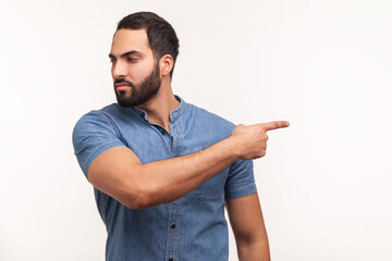 Upset angry man with beard in blue shirt pointing finger away looking with resentful expression,...