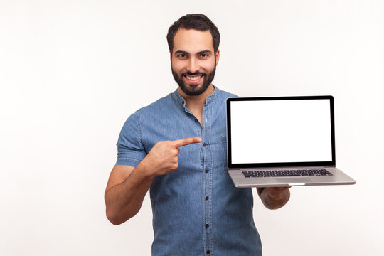 Cheerful positive man pointing finger showing empty display of laptop, blogger presenting freespace, advertising area. Indoor studio shot isolated on white background