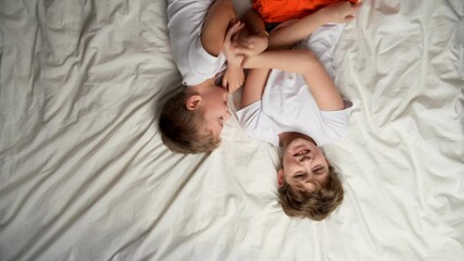 Two little caucasian boys tickling each other and laughing lying in bed. Brothers having fun, fooling around at home.