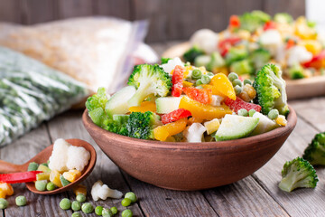 Frozen vegetables: a mix of vegetables in a bowl on wooden table. Close-up with a copy space. Horizontal orientation.
