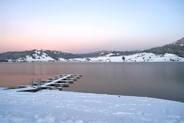 Sunset on Lake Sihl, or Sihlsee in German, in village Gross, Switzerland on a winter day. the mountains reflect on water surface their shape and colors, the moon is already on the sky. 
