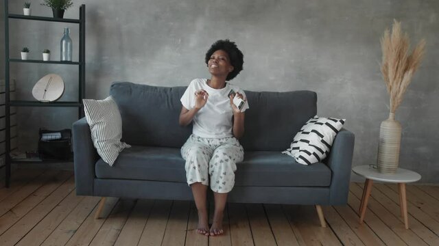 African American girl dancing with her phone on the couch in a cozy room