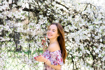 Waist up portrait of young smiling woman with red hair near blossoming plum tree