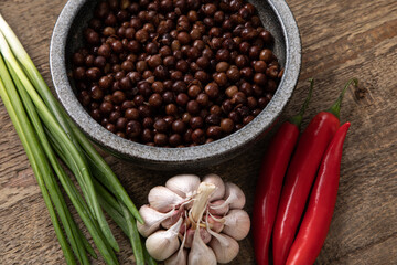 Grey peas in round  bowl on wooden table with garlic, chilli and onions next to it 
