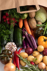 flat lay view of fruits and vegetables spilling out of a paper bag onto white counter top