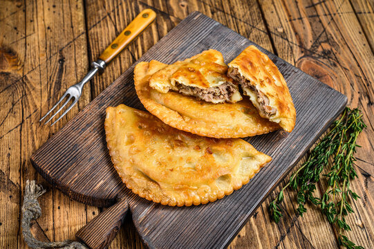 Chilean fried empanadas filled with minced beef meat served on a wooden cutting board. Wooden background. Top view