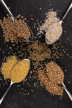 Four tablespoons full with different grains placed on black slate shot from top   