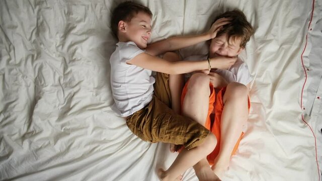 Two little caucasian boys fooling around lying in bed. Top view. Brothers having fun.