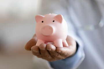 Close up focus on piggy bank in doctor hands. Money savings for family healthcare private services, medical insurance payments, clinic laboratory analyzes fees, hospital budget accounting, medicare.
