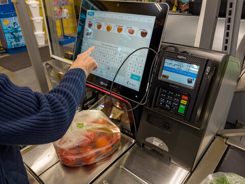 NORTH PORT, FLORIDA - January 10, 2021 : Female shopper using self service checkout at grocery store. Customer scanning produce items using supermarket self serve cash register.