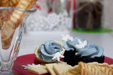 Muffin with cream cheese cream. Decorated with a marshmallow snowflake. Nearby waffle cones and ingredients for their preparation.