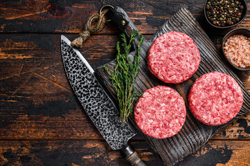 Raw steak burgers patties with ground beef and thyme on a wooden cutting board. Dark Wooden background. Top view. Copy space