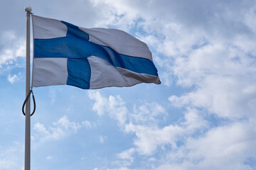 The flag of Finland with a blue sky and clouds in the background.