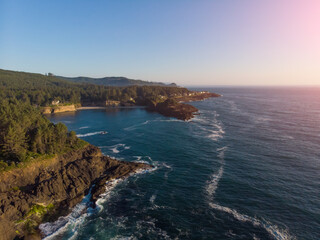 Aerial drone panoramic view of rocks in the ocean waves. Rocky coast with green plants. Beautiful sunny weather. Amazing natural landscape. View from above. Wallpaper design.