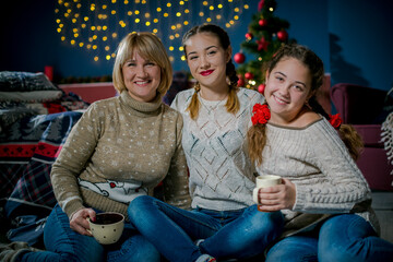 Mom and daughters are at home in winter. Family have fun together in the bedroom in winter. Mom with a cup sits and looks at the camera, children laugh in the bedroom interior