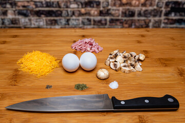 Diced Mushrooms and ham with cheese and eggs, salt, pepper and dill, on a wooden cutting surface with a knife.