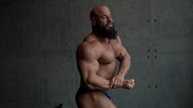 strongman with muscular body is posing for camera in studio, demonstrating figure