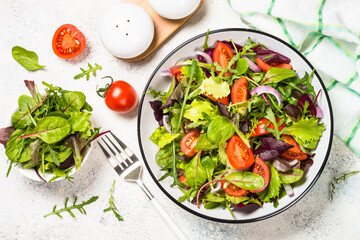 Green salad from fresh salad leaves and vegetables in white plate. Healthy vegan food. Top view image.
