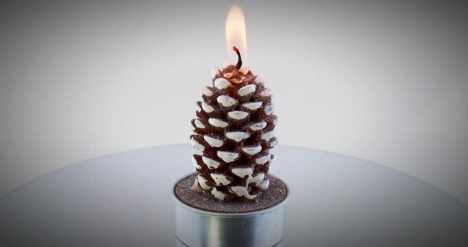 Burning pinecone shaped tee candle on spinning lazy susan turntable. 4k video