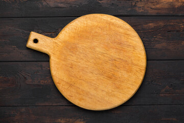Round wooden cutting board for pizza ondark wooden background. Top view. Mock up for food project.