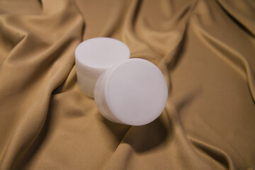 Fototapeta na wymiar mpty white plastic jar with cream or gel. Closed round jar on a beige fabric background.