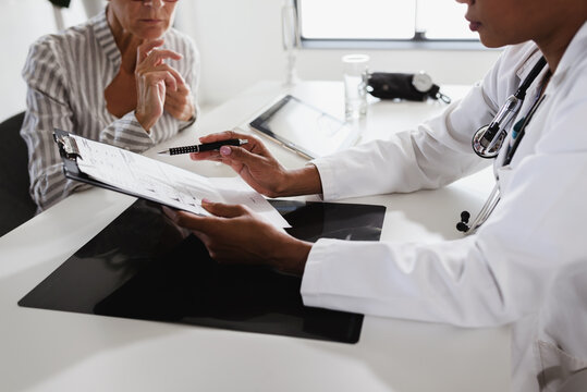 Female Doctor Looking At Test Results Of Her Patient. Doctor And Patient Talking Over A Medical Test Result.