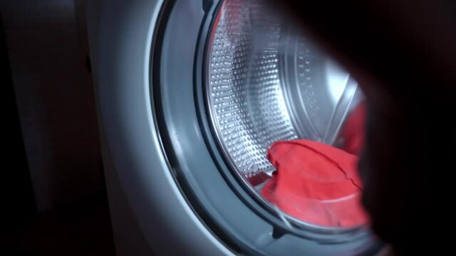 Housewife throwing three chemical double concentrated detergent granules in transparent shell inside the spinning drum of washing machine, process of loading dirty clothes for washing. Eco clener and