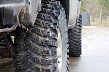 front wheel of off-road vehicle with rough tread pattern of car tire with mud close up on blurred background
