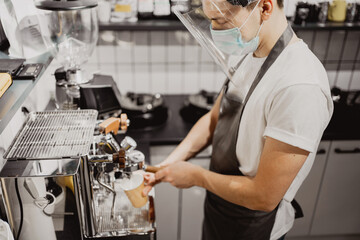 A barista wearing a virus mask. professionally brews a fragrant cappuccino Americano for the client. A stylish Italian coffee machine in the cafe prepares coffee to take away. 