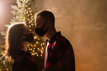 A young couple man and woman in disposable medical masks under a Christmas tree.