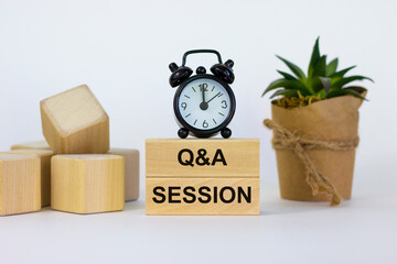 Q and A, questions and answers session symbol. Concept words 'Q and A session' on wooden blocks on a beautiful white background. Black alarm clock, house plant. Business and Q and A session concept.