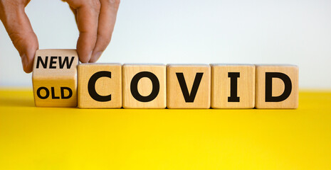 Mutated covid symbol. Male hand turns a cube and changes words 'old covid' to 'new covid'. Beautiful yellow table, white background. Medical and mutated covid concept. Copy space.