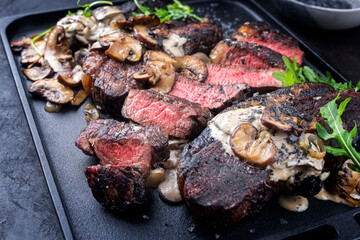 Modern style barbecue dry aged wagyu Brazilian picanha steaks from the sirloin cap of rump beef sliced and served cream sauce and mushrooms as close-up on a design tray
