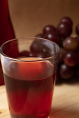 Glass cup with grape juice on wooden board and bunch of grapes in the background