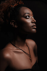 Side view of beautiful african christian woman stands on black background and looks to the spotlight. Her brow skin illuminated in light.